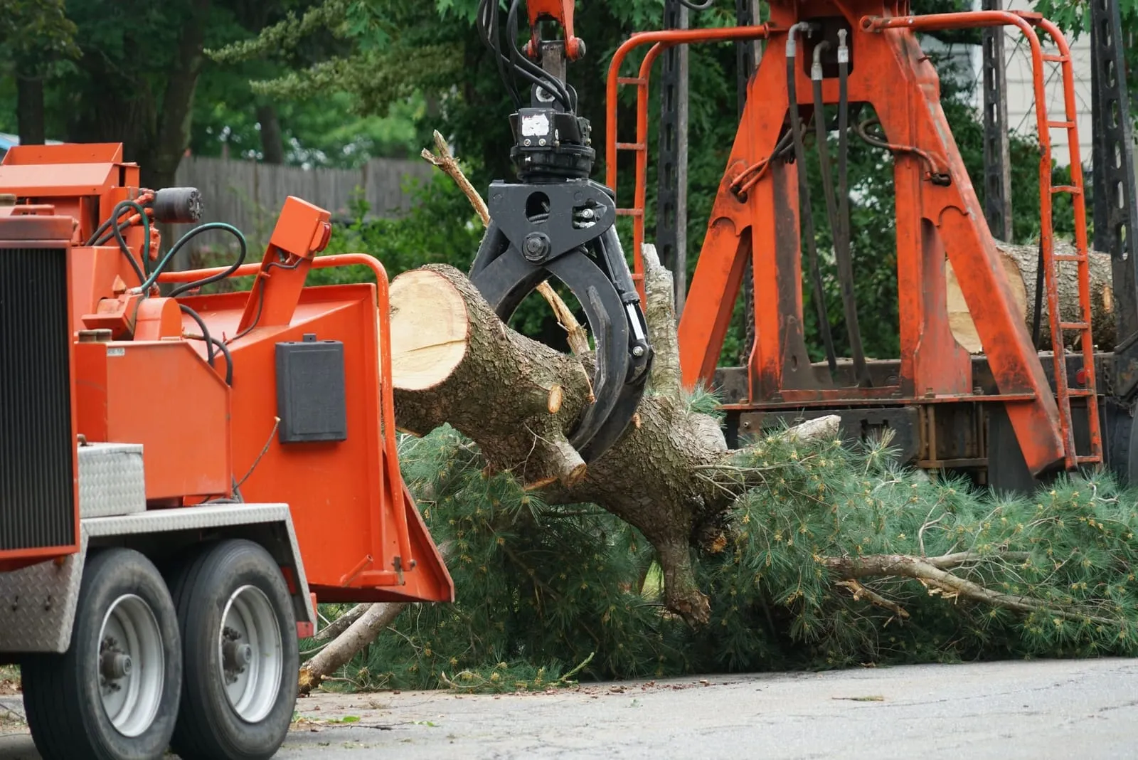 Grapple loader moving heavy tree sections next to a wood chipper during cleanup